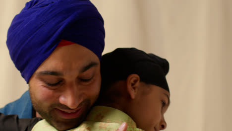 Close-Up-Studio-Shot-Of-Sikh-Father-Embracing-Son-Both-Wearing-Turbans-Against-Plain-Background-5